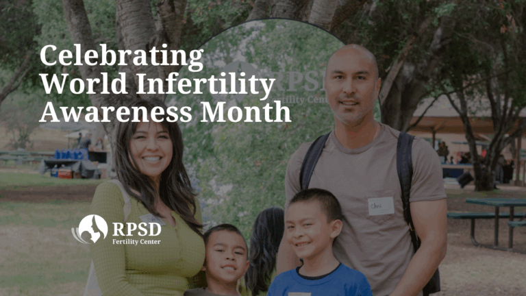 A smiling couple holding their young child in a sunlit park, symbolizing LGBTQIA+ family building and fertility success.