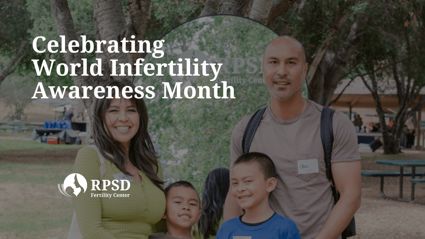 A smiling couple holding their young child in a sunlit park, symbolizing LGBTQIA+ family building and fertility success.